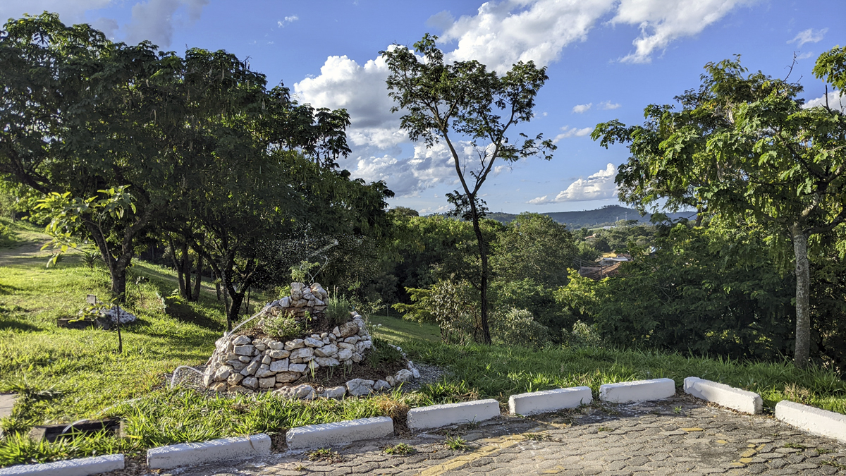 Espiral de Ervas Aromáticas na área verde em talude. Ao fundo, mata nativa. Atualmente, com pouco menos de 1 ano de idade (2024), a espiral continua despertando a curiosidade e o interesse dos transeuntes, propiciando momentos ideais para uma educação ambiental no campus durante os constantes questionamentos nos períodos de rega e manutenção, além dos pedidos de mudas (e doações para a espiral, também), elogios e críticas (que são bem vindas).